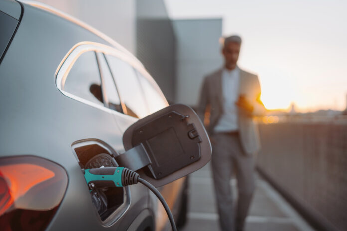 Close up of electric car charging, businessman standing in background and waiting.